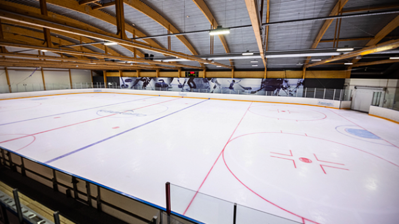 Indoor ice hockey rink with painted lines and wooden ceiling.