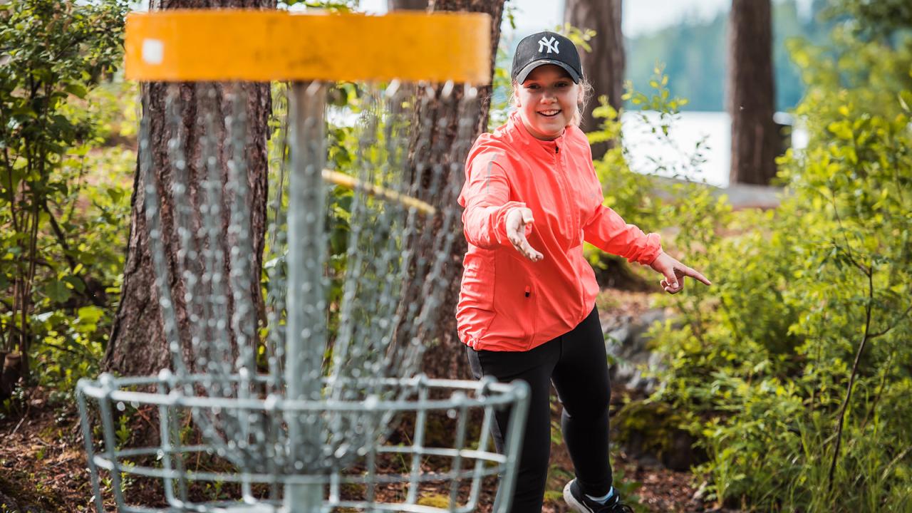 Person playing disc golf, about to throw a disc toward the target in a forest setting.