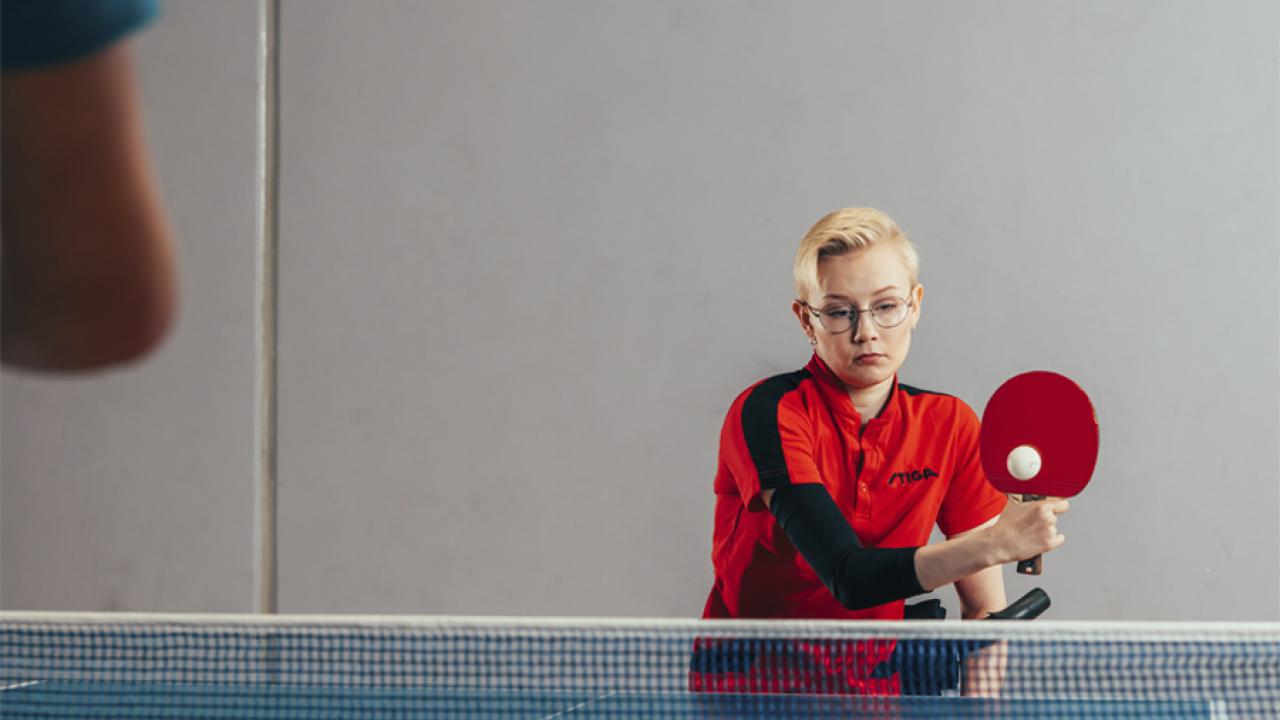 Nainen pelaa pöytätennistä punaisella mailalla.