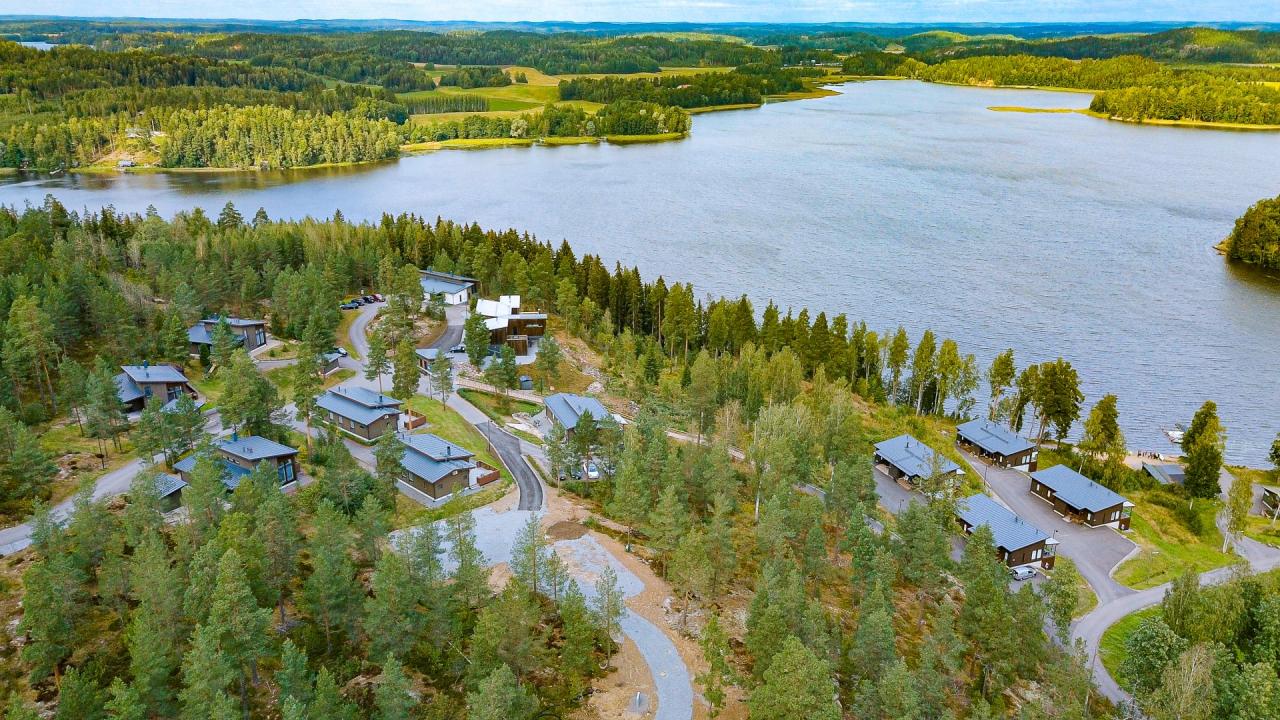 Ilmakuva metsän ympäröimästä järvimaisemasta ja mökeistä.