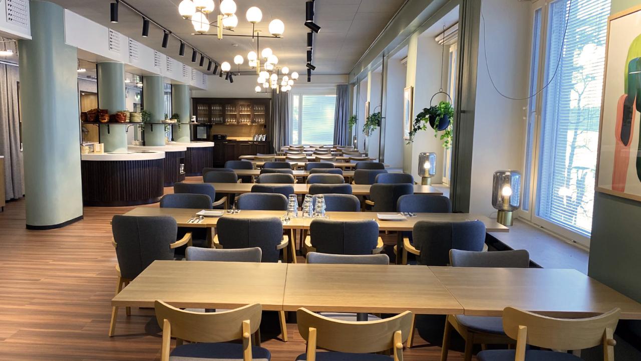 Tyylikäs ravintolasali, puupöytiä ja -tuoleja, valkoinen katto, paljon ikkunoita.