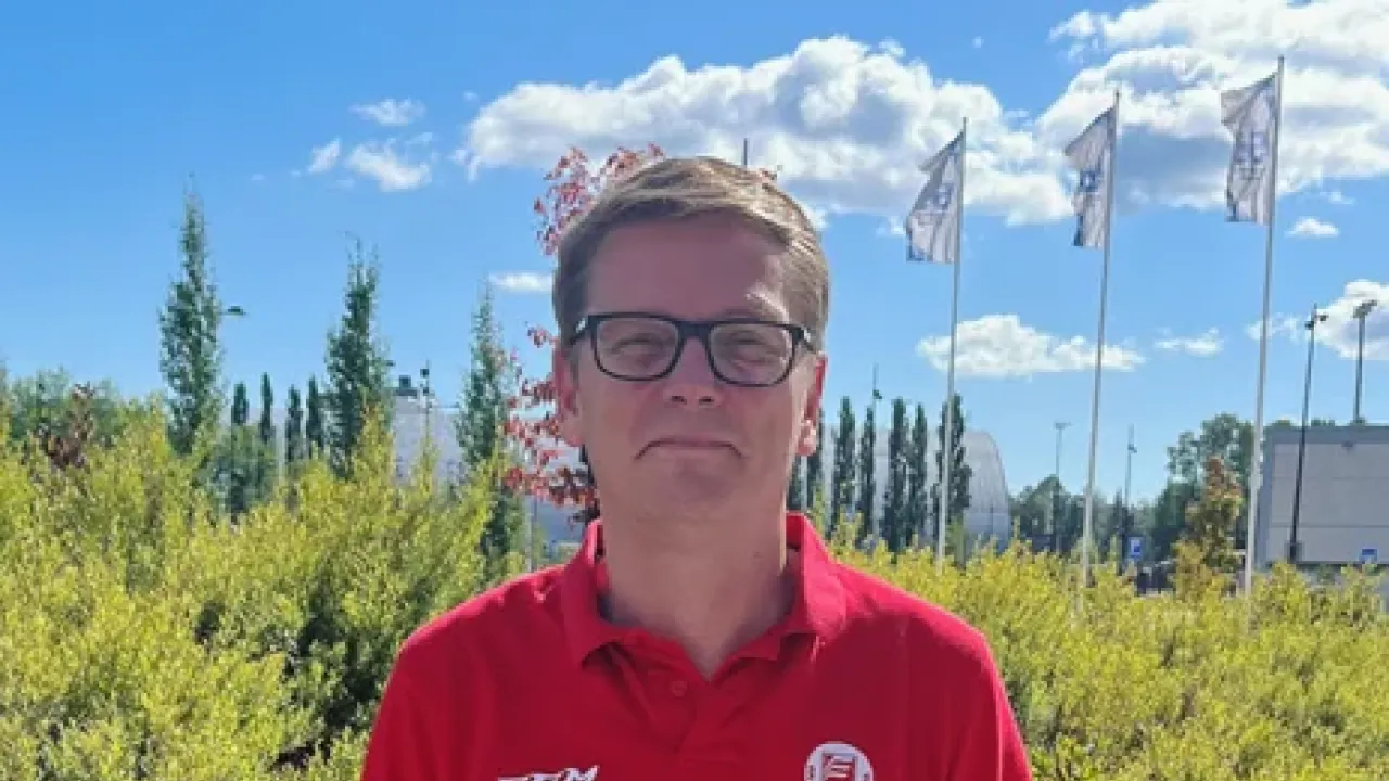 Mies punaisessa paidassa, taustalla vihreää kasvillisuutta ja sininen taivas.