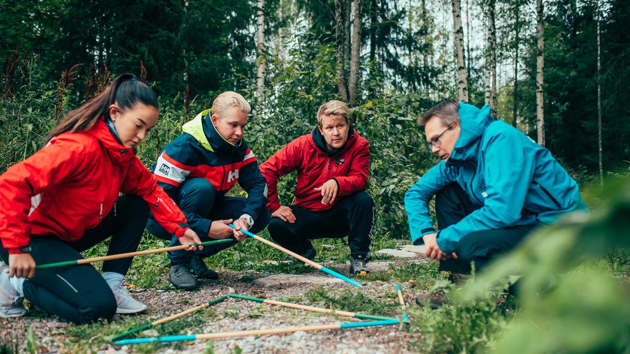 Neljä ihmistä metsässä tutkimassa karttaa kankaalla sauvojen avulla.
