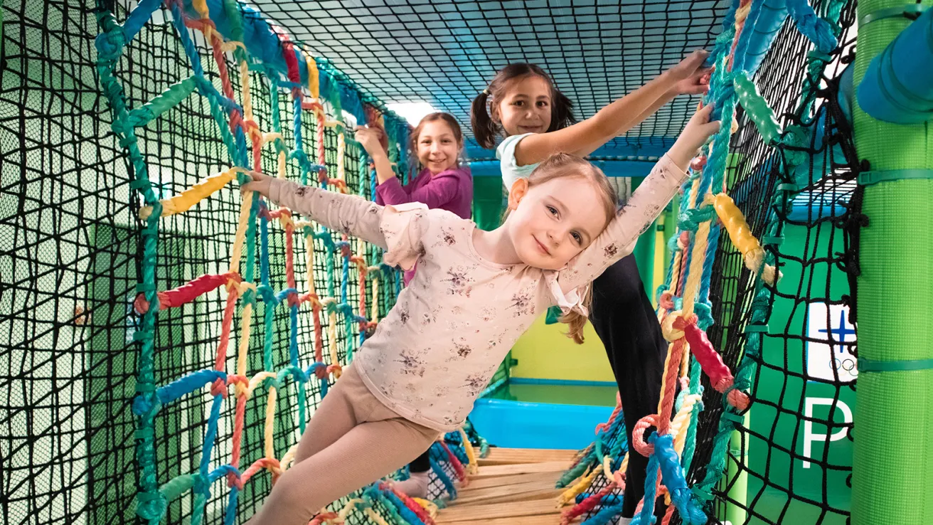 Lapset leikkivät värikkäällä kiipeilyverkolla sisätiloissa.