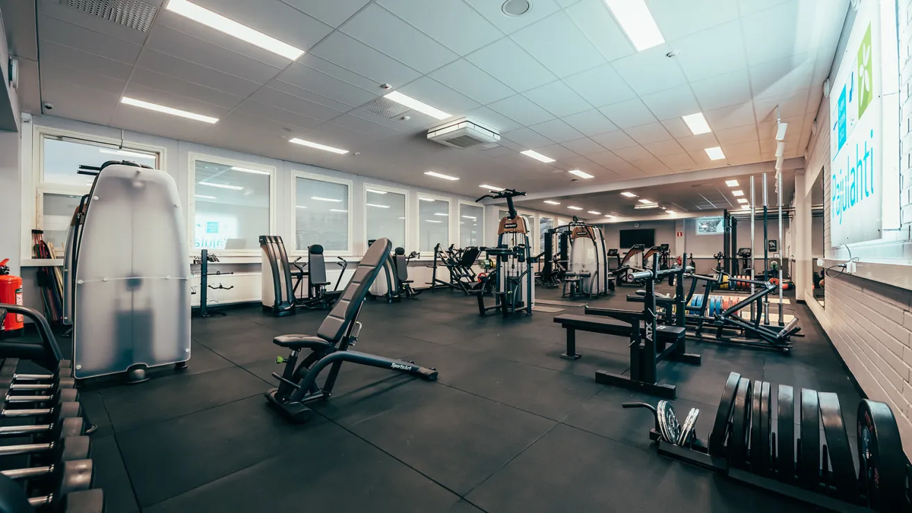 Tyhjä kuntosali, jossa on kuntolaitteita ja painoja.