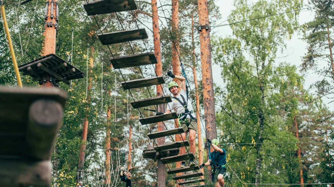 Seikkailupuistossa ihminen kävelee köysisillalla metsän keskellä.