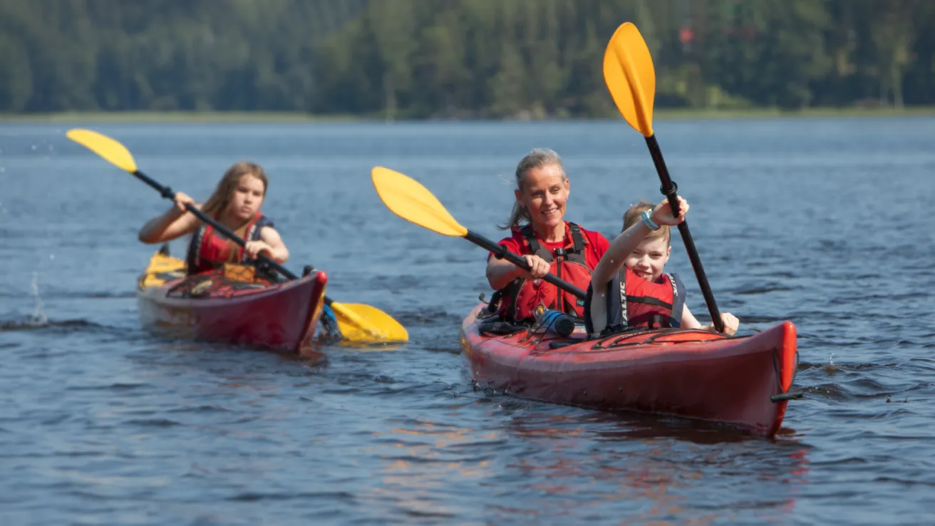 Kaksi kajakkia järvellä, aurinkoinen päivä, kaksi ihmistä kummassakin kajakissa.