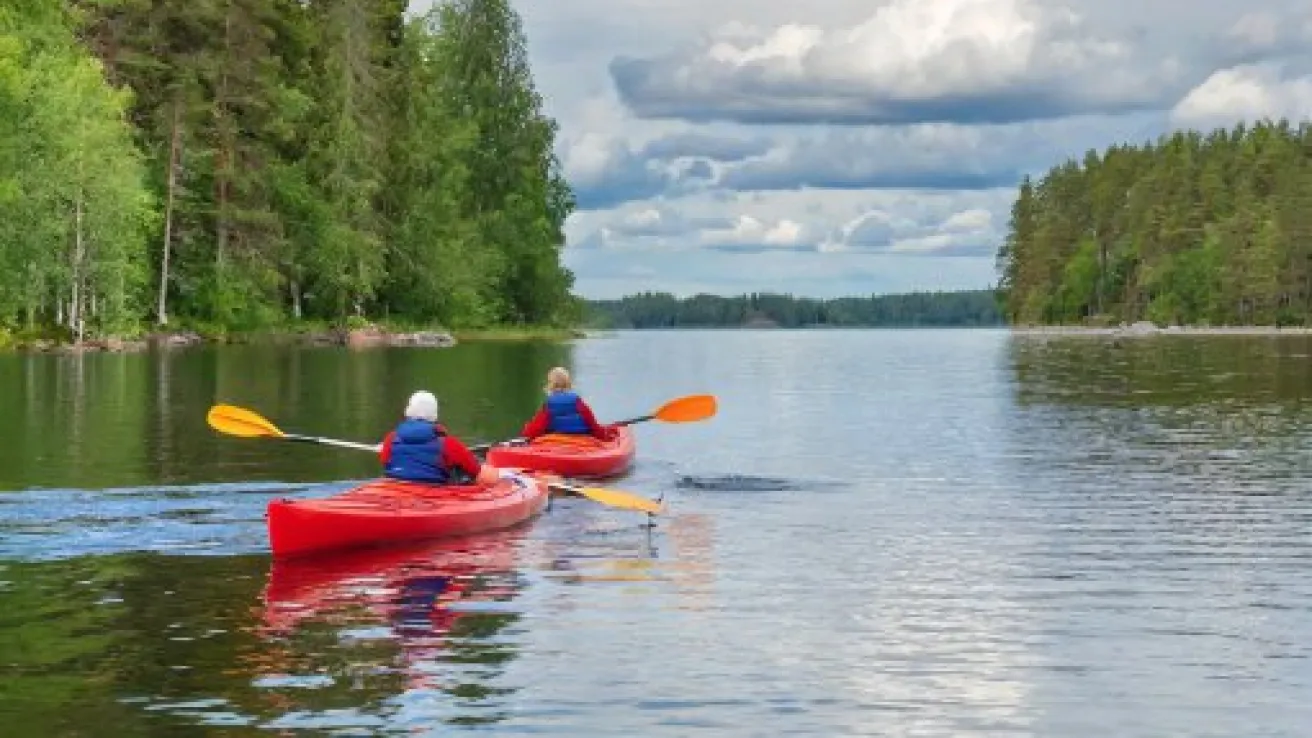 Kaksi henkilöä melomassa punaisilla kajakeilla järvellä metsän ympäröimänä.