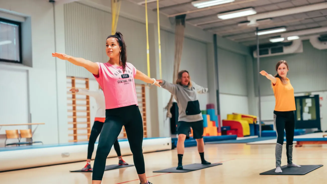 Joogaajat venyttelevät kirkkaassa liikuntasalissa.