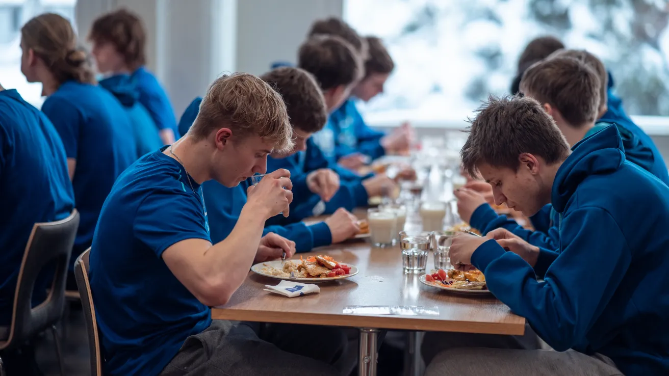 People in blue shirts eating at a communal table indoors.