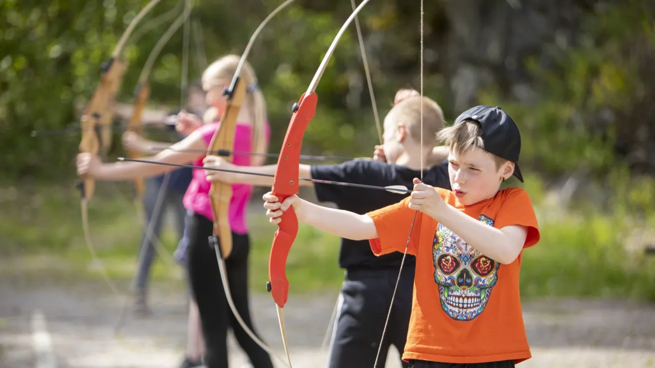 Lapsia jousiampumassa ulkona, keskittyneet ilmeet.