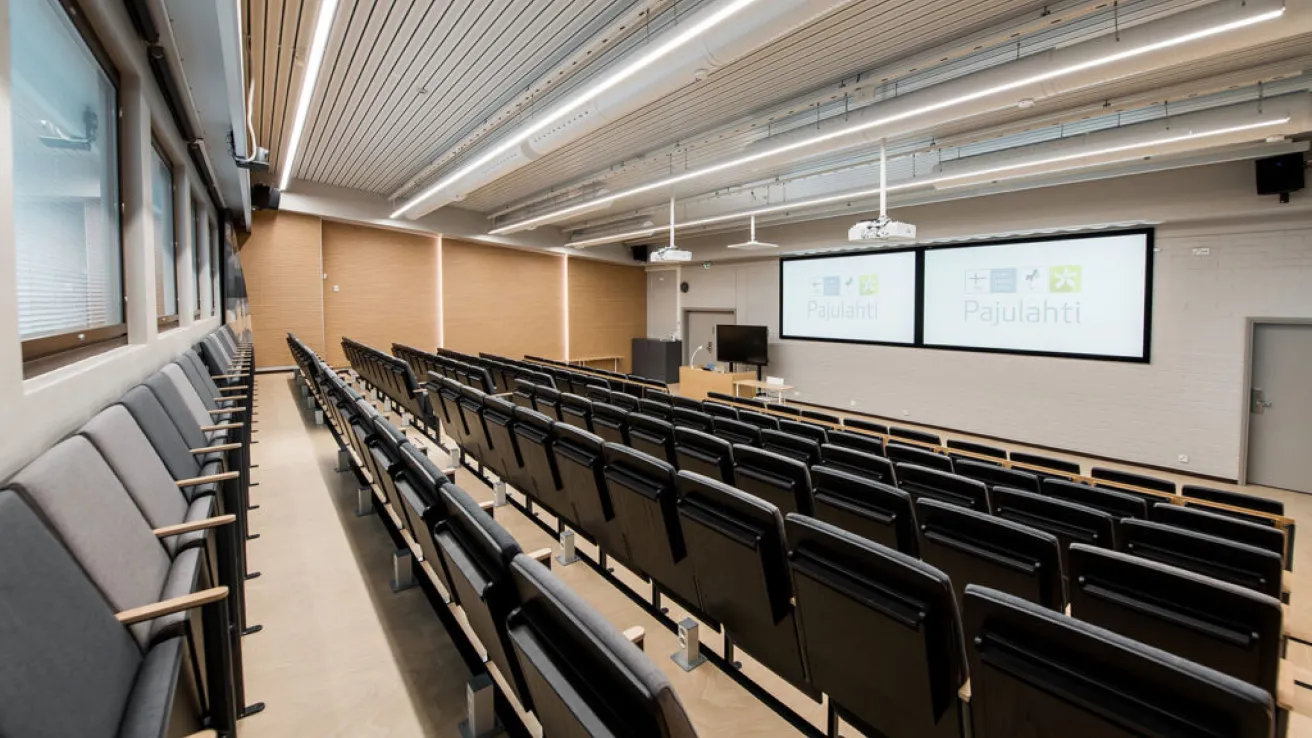 Tyhjä nykyaikainen luentosali, jossa on rivissä tuoleja ja kaksi näyttöä edessä.