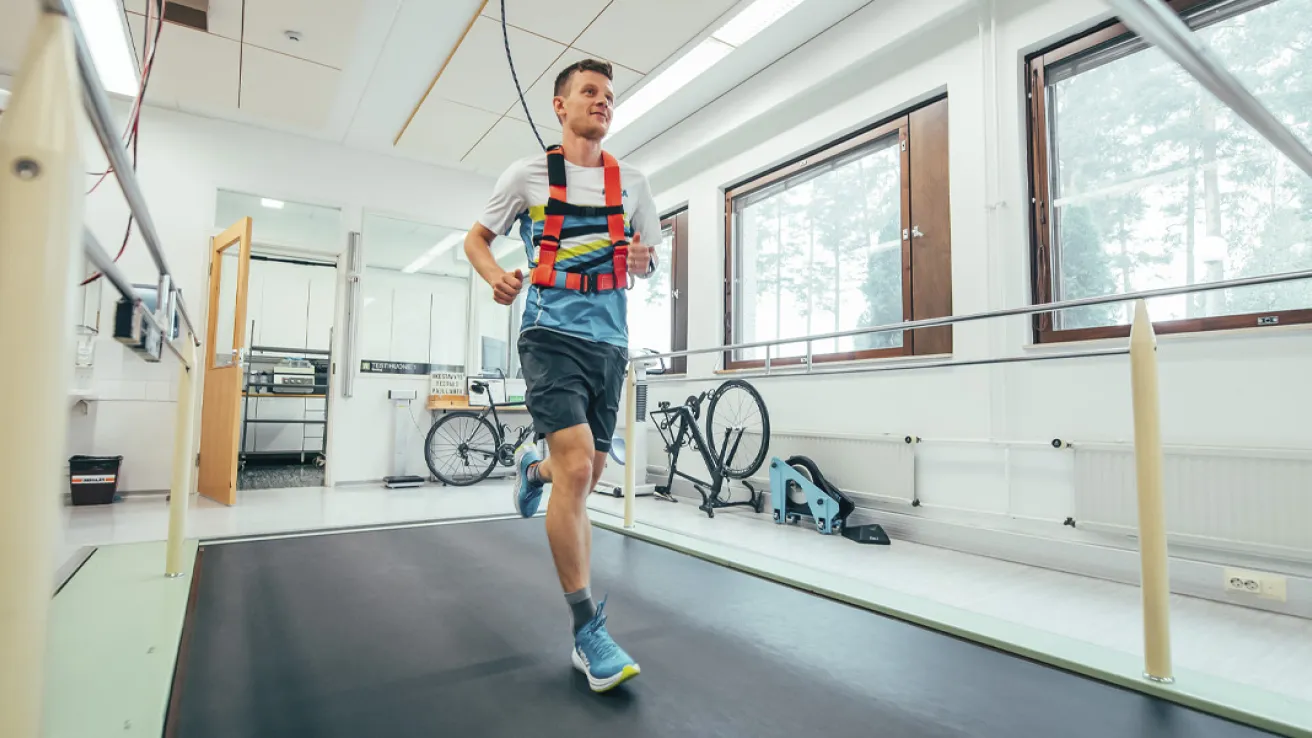 Mies juoksee juoksumatolla vaaleassa huoneessa, taustalla polkupyöriä.