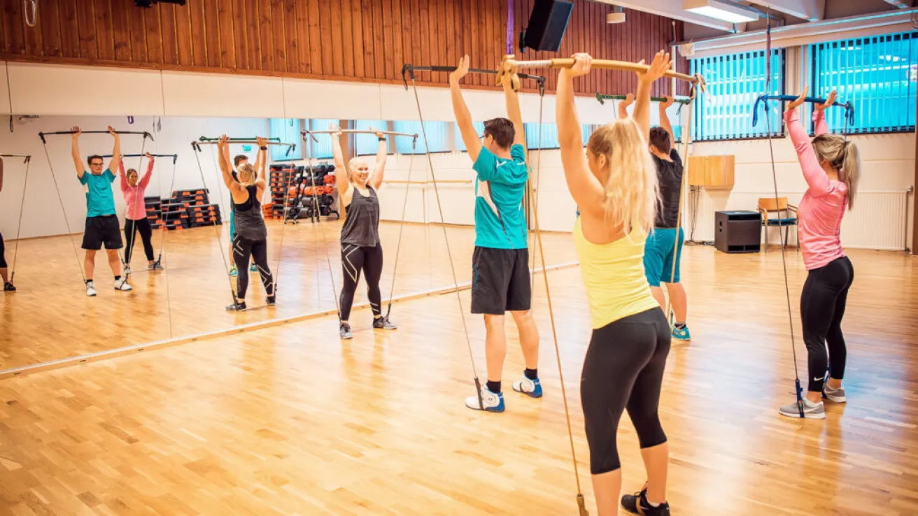 Treeniryhmä seisoo peilisalissa nostaen painotankoja ilmaan.