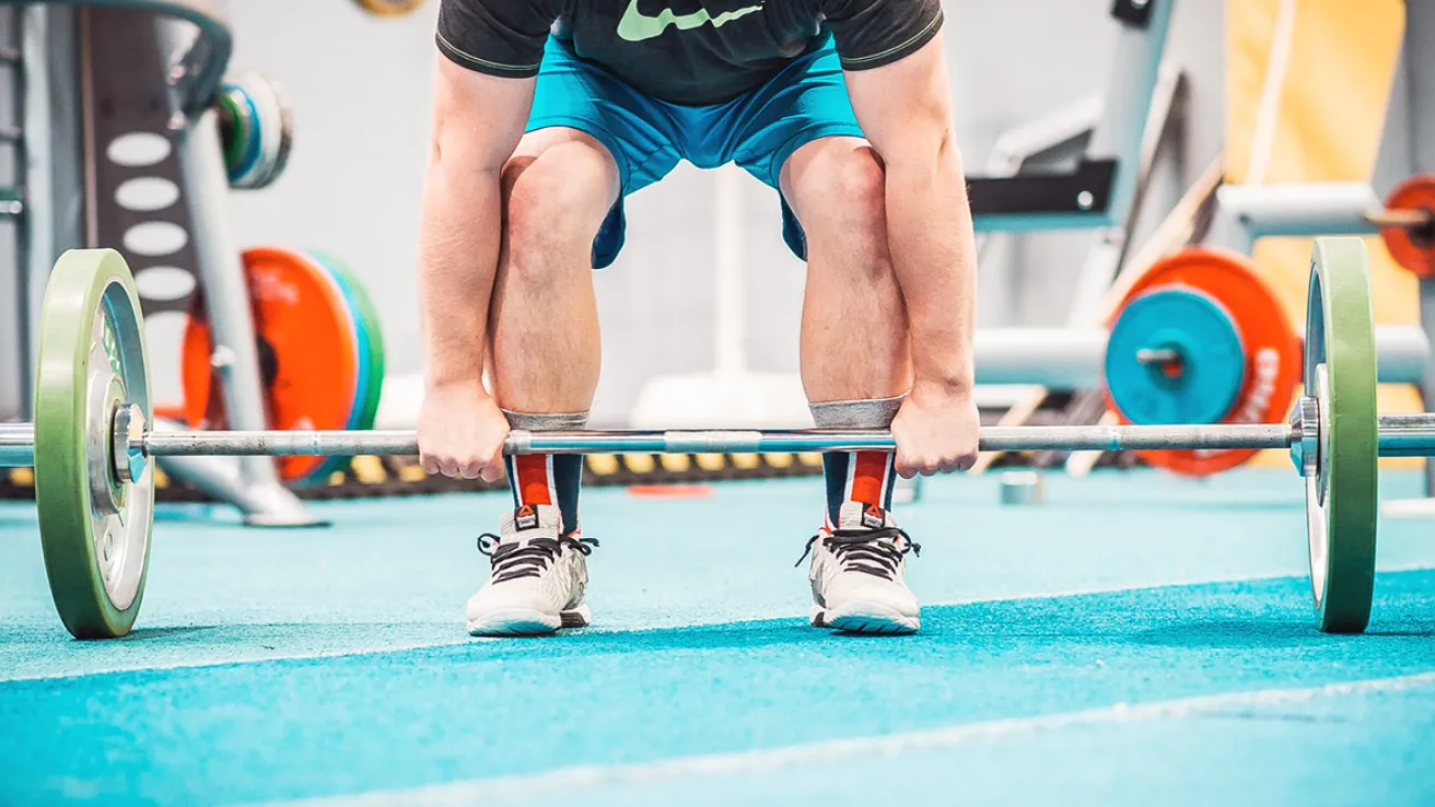 Mies nostaa painonnostotankoa kuntosalilla.