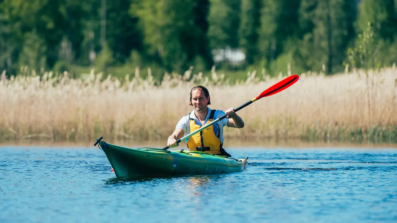 Mies meloo vihreässä kajakissa järvellä, taustalla metsää ja kaislikkoa.