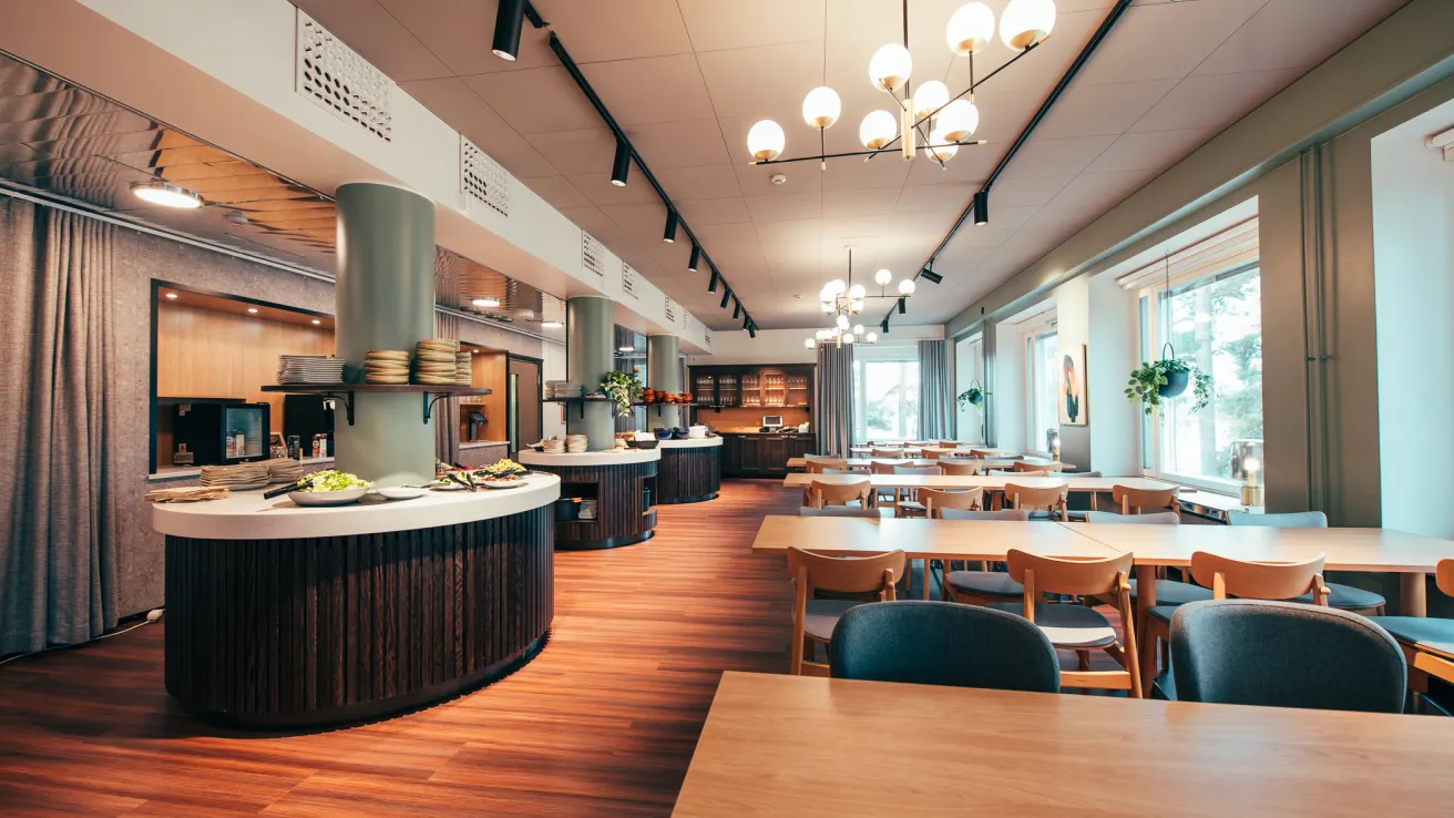 Tilava, valoisa ja moderni ruokailutila puupöydillä ja isoilla ikkunoilla.