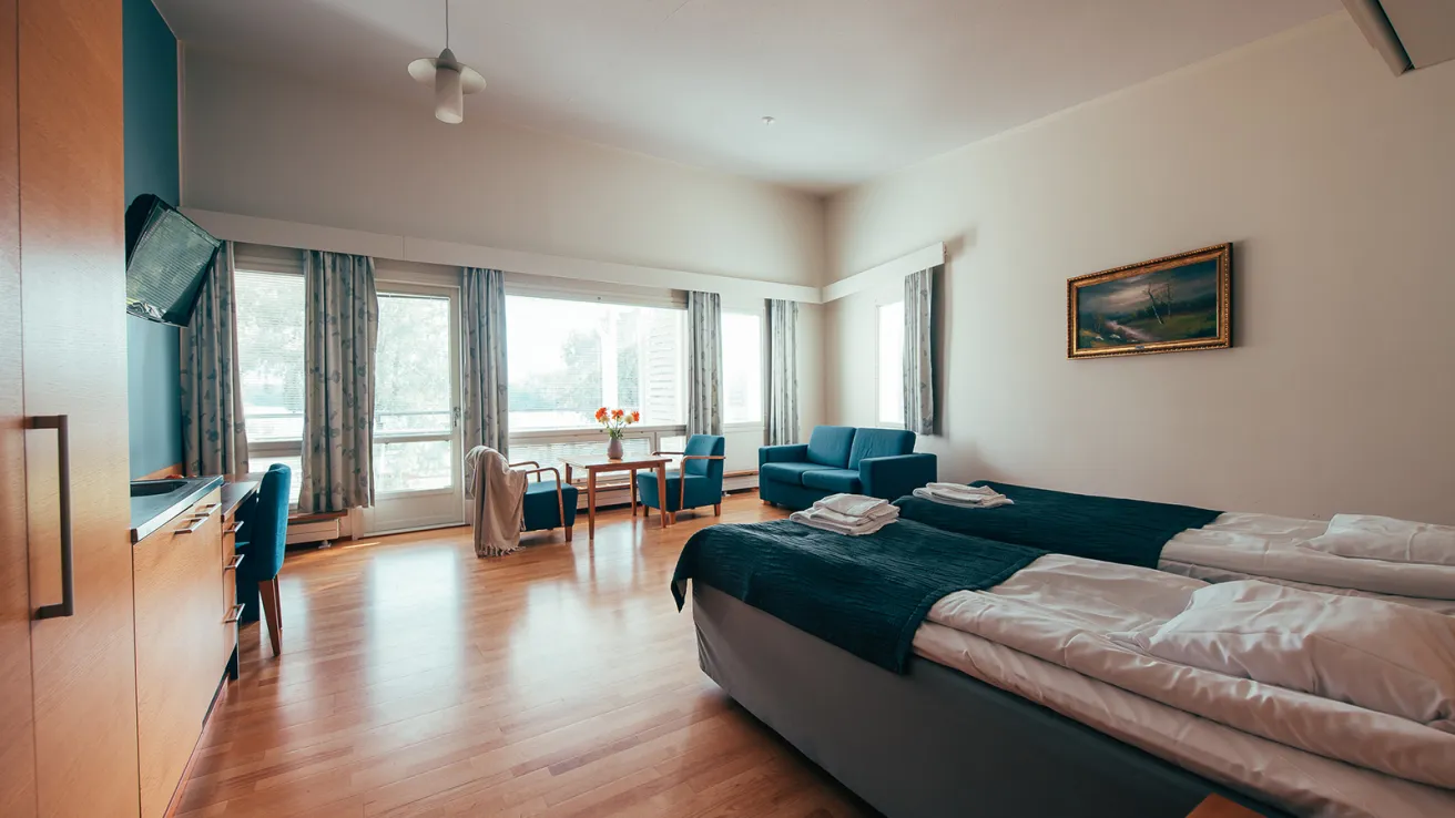 Tilava hotellihuone, kaksi sänkyä, sohva ja suuri ikkuna.