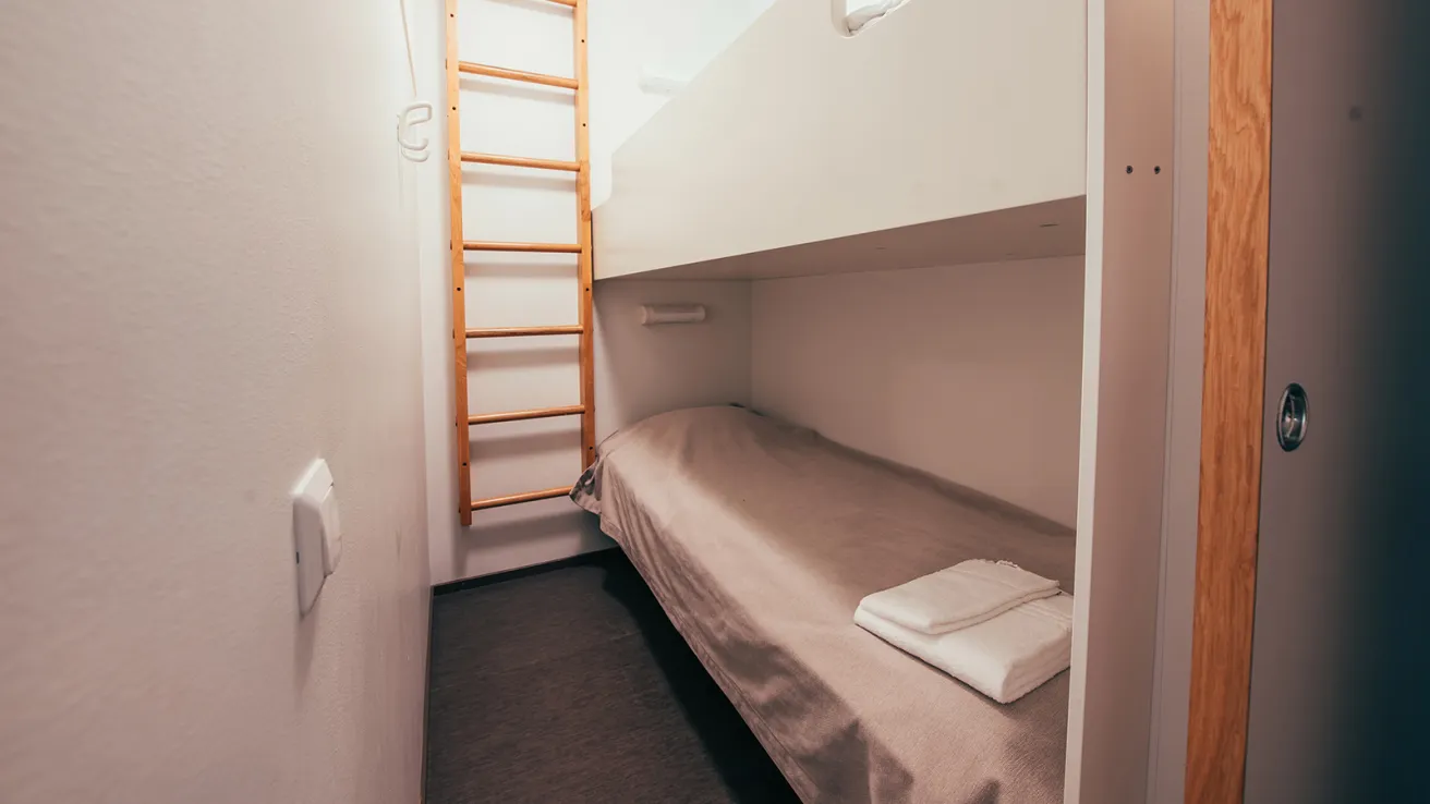 Kaksi kerrossänkyä pienessä huoneessa, alemmalla sängyllä valkoinen pyyhe.