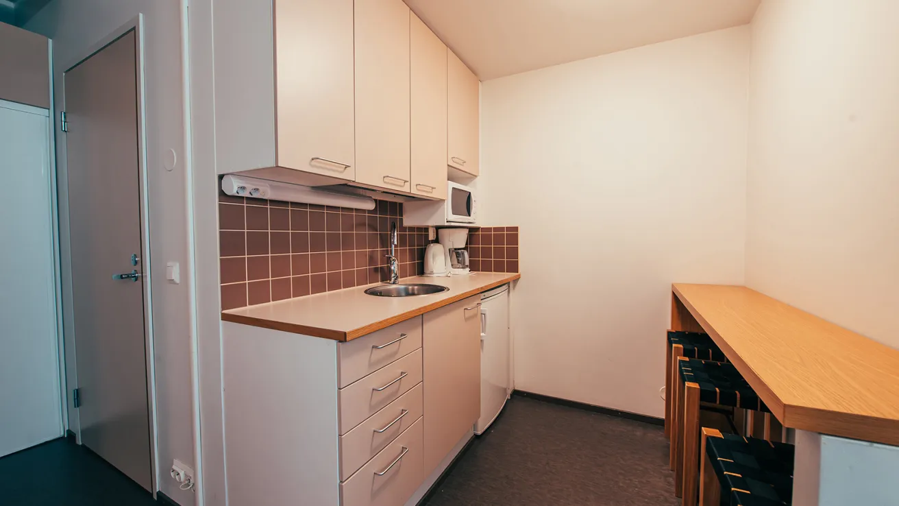 Pieni keittiö, vaaleat kaapit ja ruskea laattaseinä.