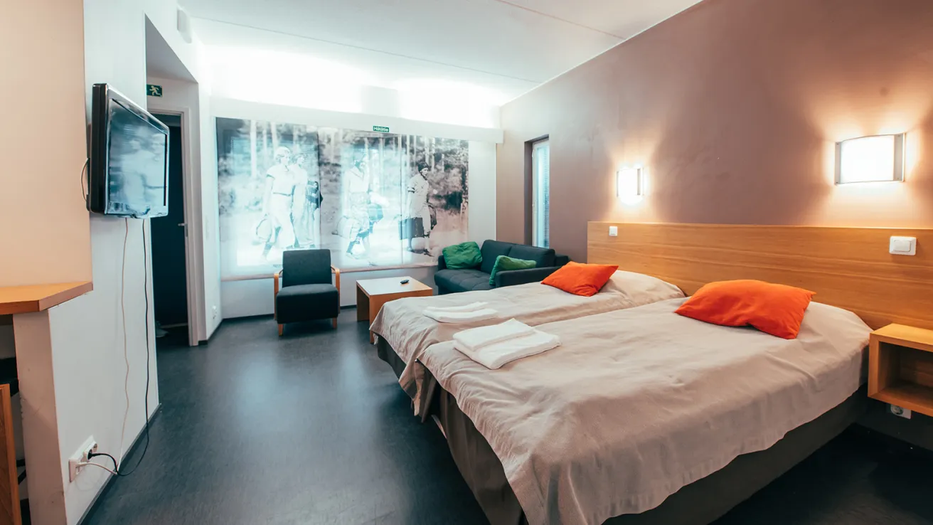 Moderni hotellihuone kahdella sängyllä, seinällä taulu ja TV.