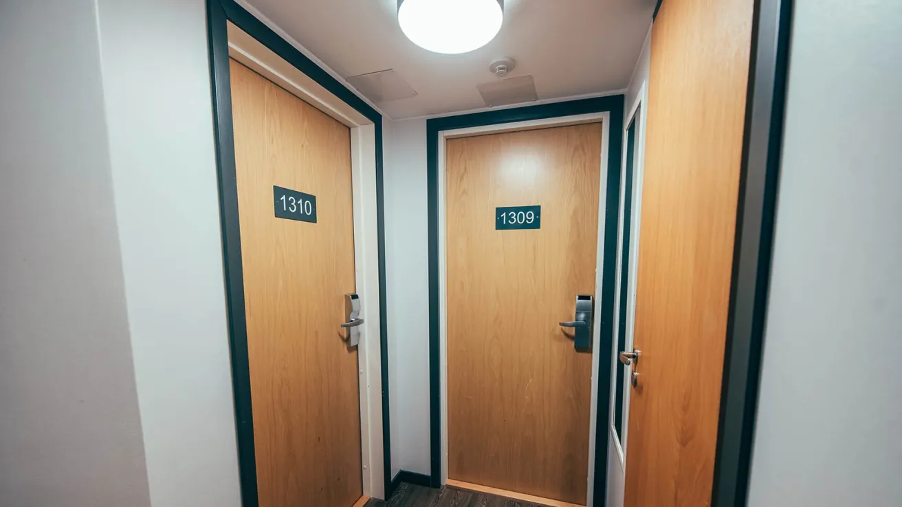 Kapea käytävä, jossa kolme puuovea ja huonenumerot.