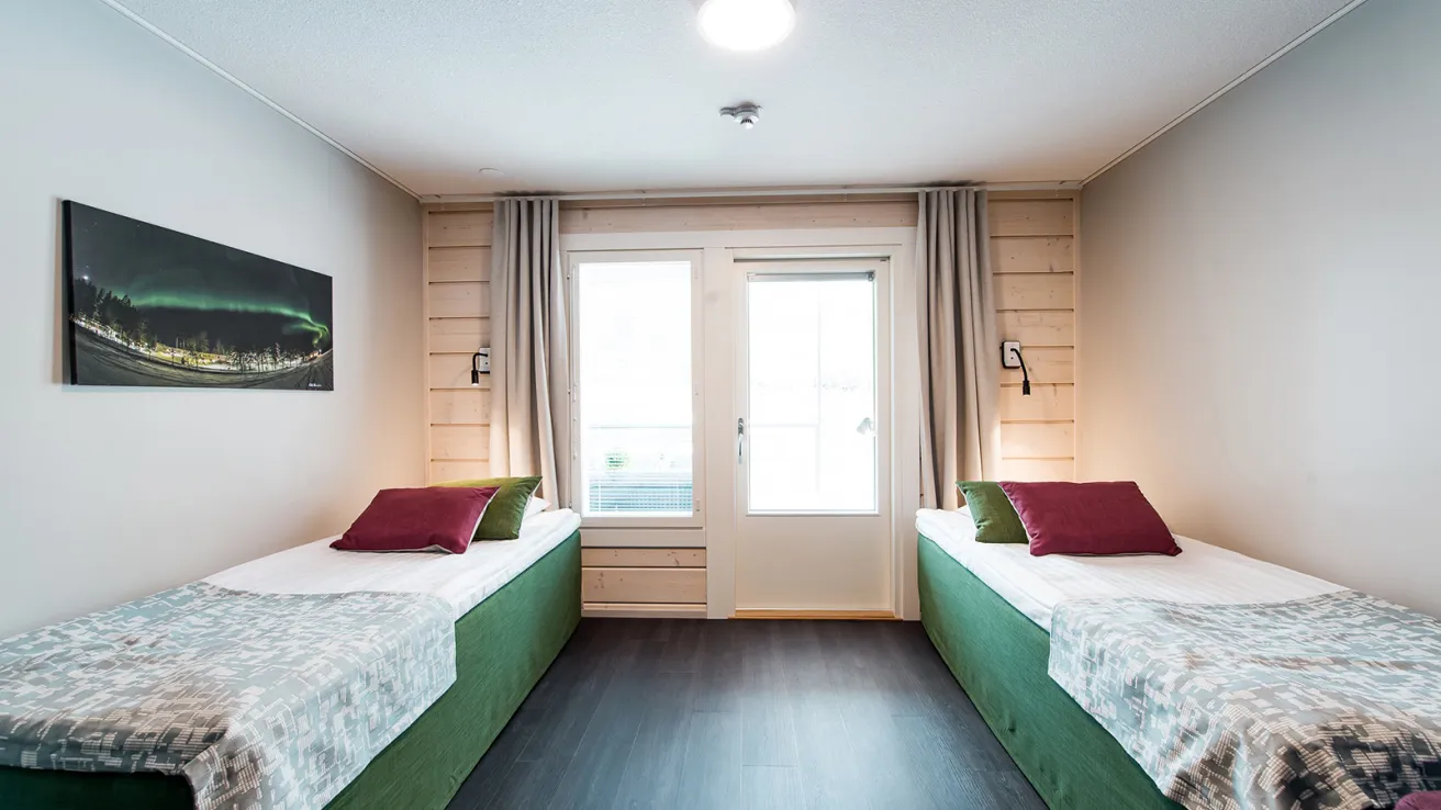 Kaksi yhden hengen sänkyä vaaleassa huoneessa, ikkunasta näkyy valoisa taivas.