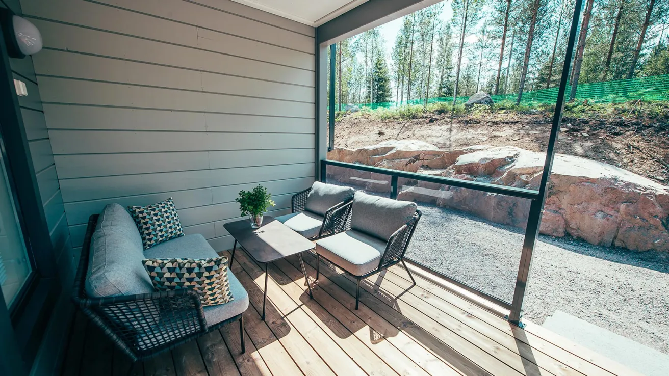 Veranta, jossa sohva, kaksi tuolia ja pöytä; taustalla metsä.