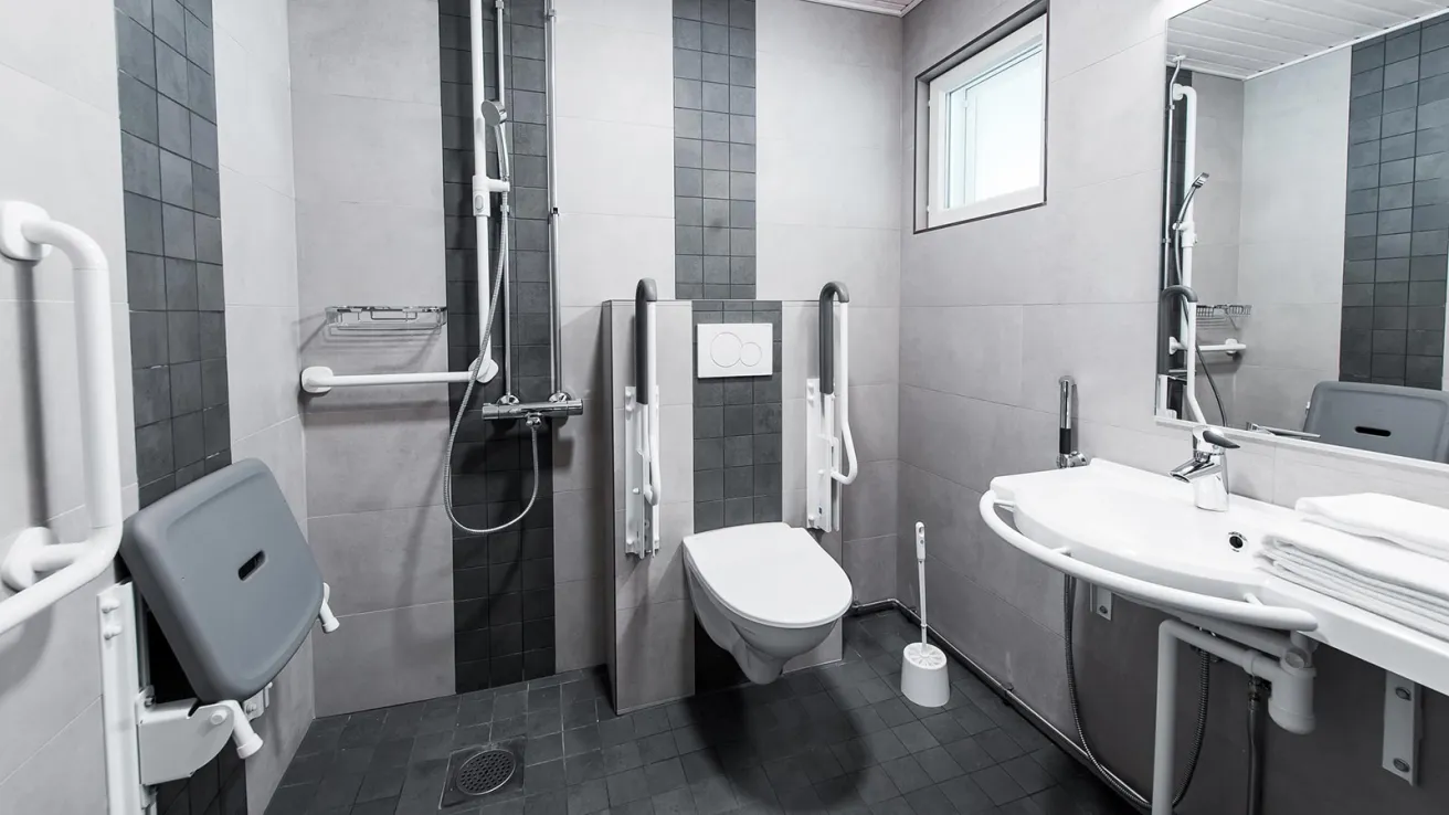 Esteetön kylpyhuone, jossa on suihku ja wc-tukikaiteineen.