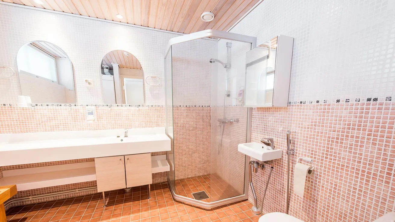 Tilava kylpyhuone, suihkukaappi, kaksi pesuallasta, vaaleanpunainen lattia.