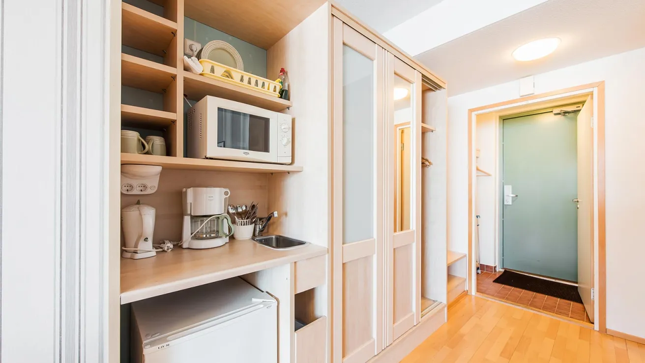 Pienkeittiö, vaalea puu, mikroaaltouuni, jääkaappi, kahvinkeitin, valoisa tila.