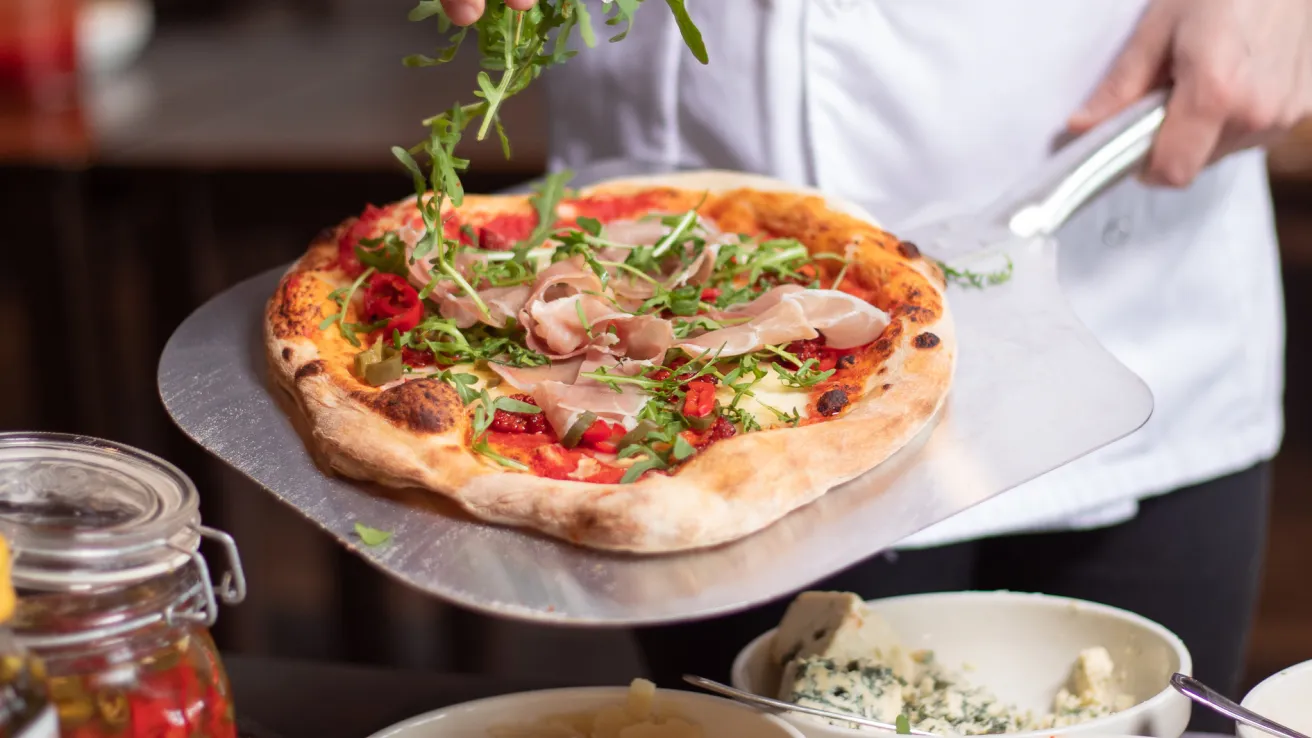 Kokki lisää pizzan päälle rucolaa keittiössä.