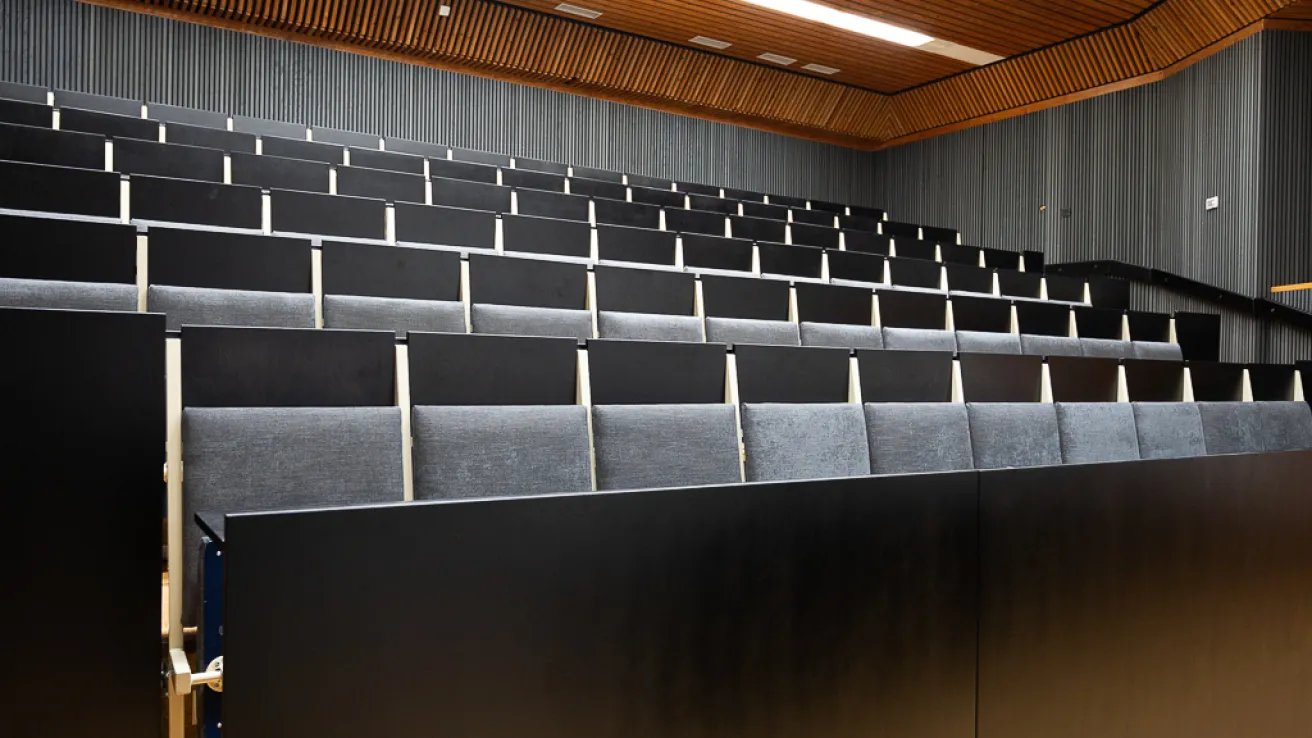 Tyhjä auditorio, mustat penkkirivistöt ja puinen katto.