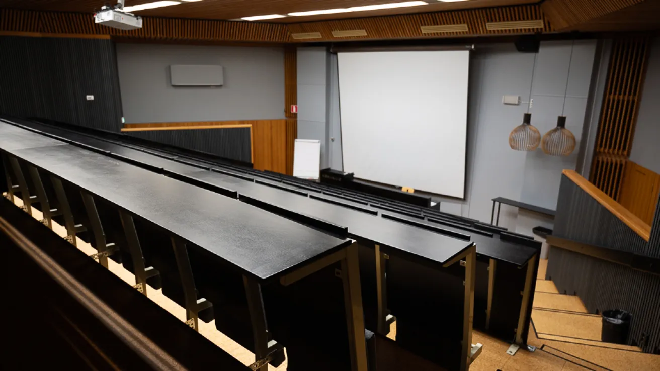 Tyhjä auditorio, valkotaulu ja projektori, tummat penkit.