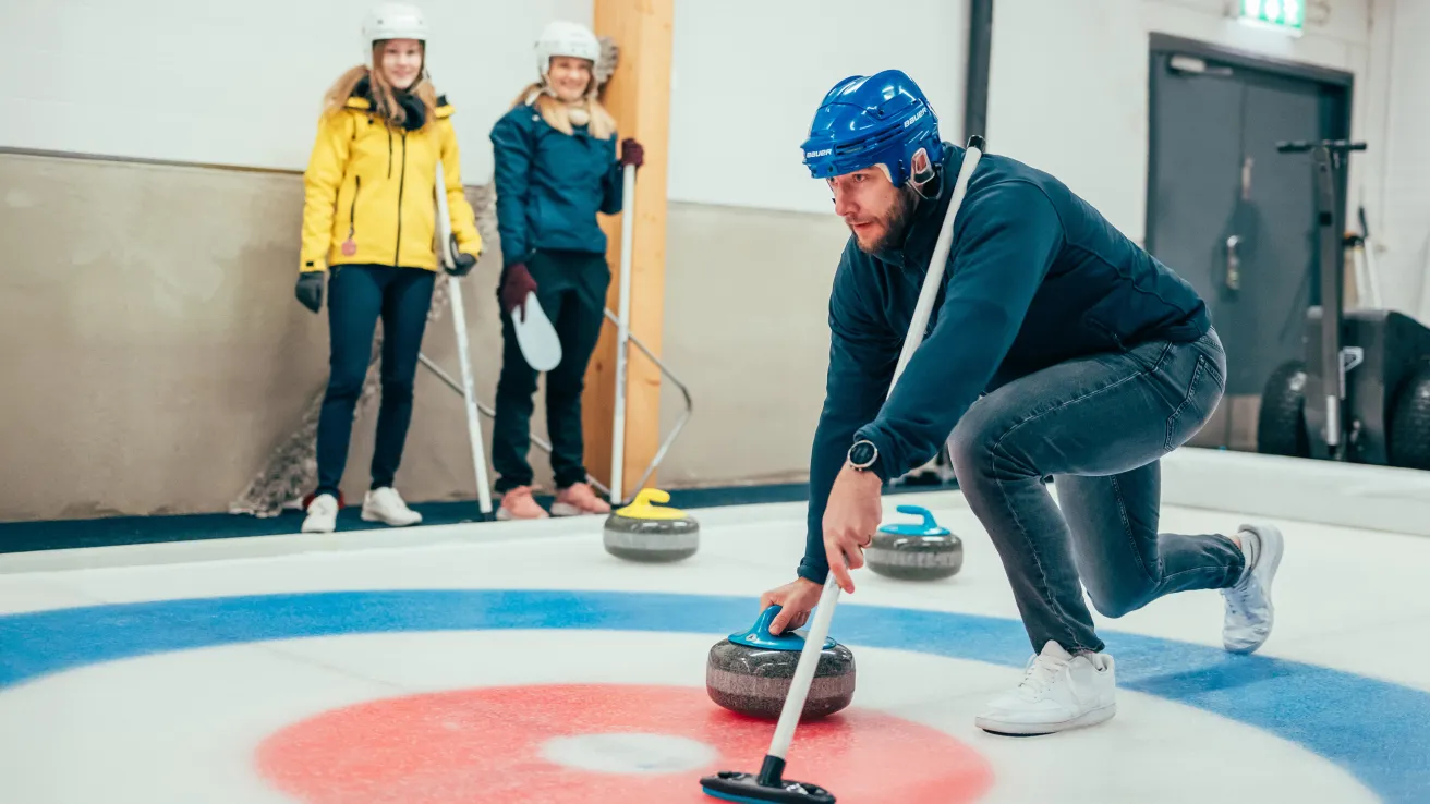 Kisakallion jäähallissa mies on jäällä työntämässä curling-kiveä.