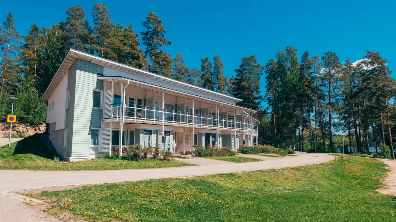 Hopeapaju. Kaksikerroksinen talo metsäisessä ympäristössä, kirkas sininen taivas.