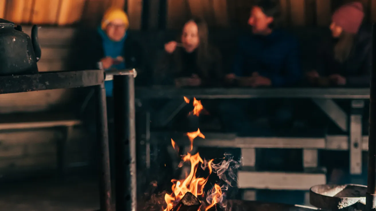 Suurkodassa on nuotio ja taustalla ihmisiä syömässä.