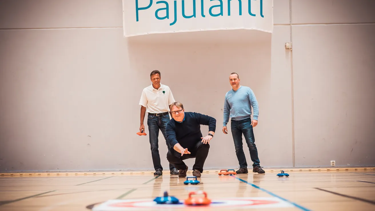 Sisäcurlingia pelaa kolme miestä, joista yksi työntää kiveä.