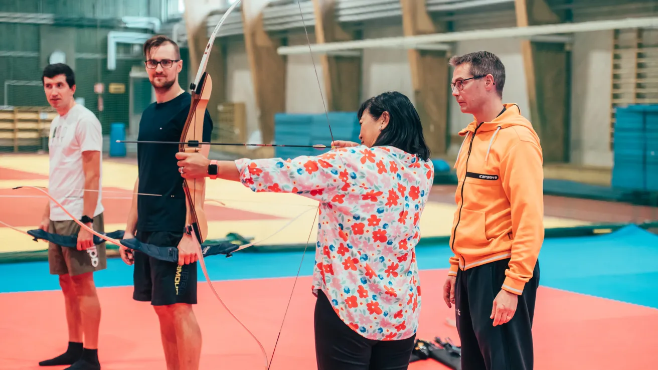 Ohjaaja opettaa ryhmälle jousiammuntaa.