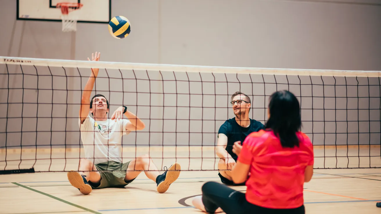 Paralajissa istumalentopallossa mies istuu lattialla verkon takana ja on lyömässä palloa.