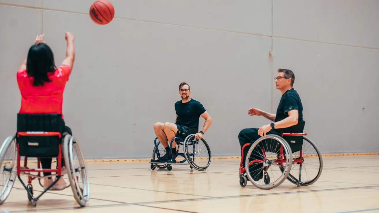 Paralajissa pyörätuolikoriksessa nainen pyörätuolissa heittää palloa kohti pyörätuolissa istuvaa miestä.