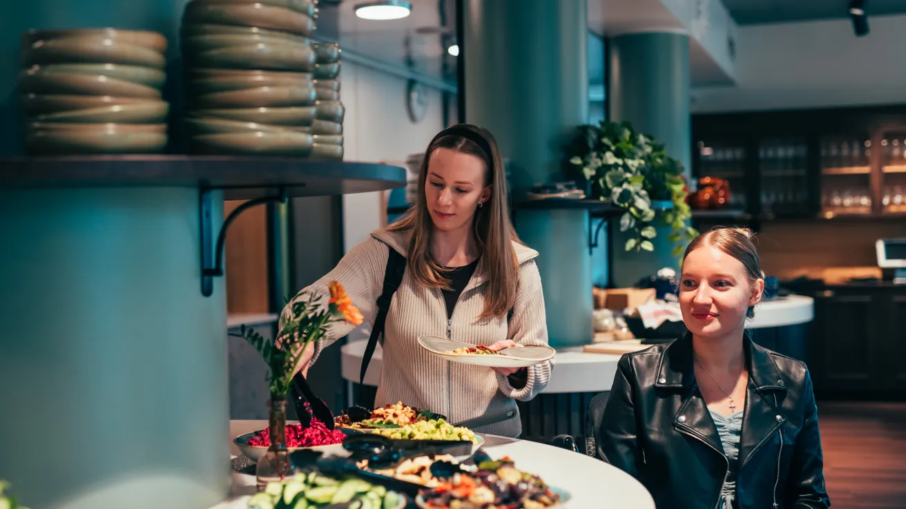 Ravintola Fannissa pyörätuolissa istuva nainen ja hänen avustajansa ottavat ruokaa lautaselle tarjoilupöydältä.