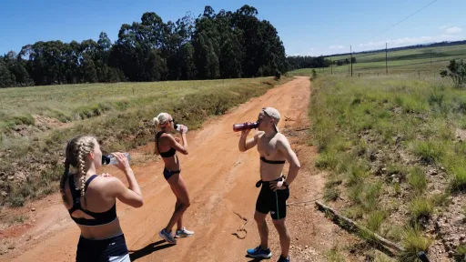 Kolme ihmistä juoksevat hiekkatiellä, juoden vettä auringonpaisteessa.