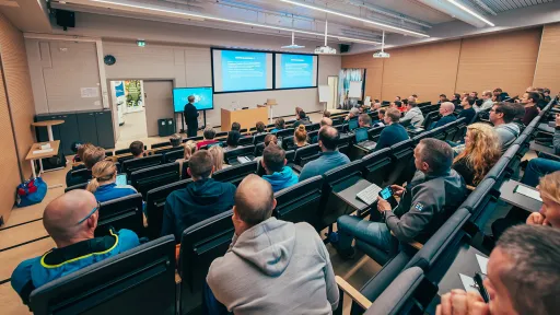 Lecture hall with audience facing a speaker and projected slides.