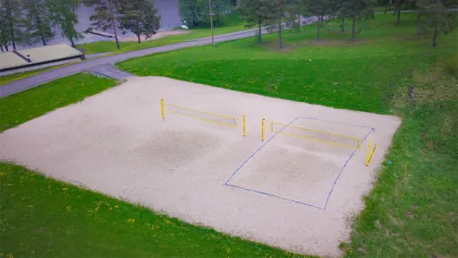 Hiekkapohjainen lentopallokenttä puistossa, vihreää nurmikkoa ympärillä.