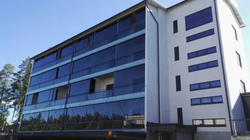 Kerrostalo, jossa on lasiseinä ja parkkitila alhaalla, kirkkaassa auringonpaisteessa.