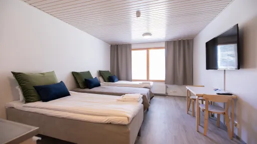 Kaksi vuodetta, pöytä, tuolit ja televisio vaaleassa huoneessa.