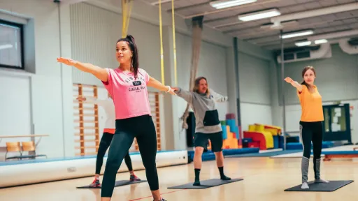 Joogaajat venyttelevät kirkkaassa liikuntasalissa.