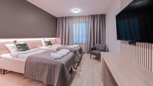 Kaksi sänkyä hotellihuoneessa, iso televisio seinällä.