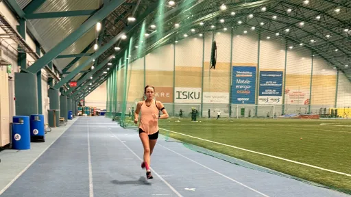 Juoksija sisäurheiluhallissa sinisellä juoksuradalla.